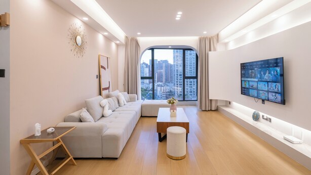 A modern living room with a sofa, a coffee table, a TV, and a large window with a city view.