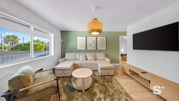 Una sala de estar moderna con un sofá modular, una mesa de centro redonda y un televisor de pantalla plana grande montado en la pared.