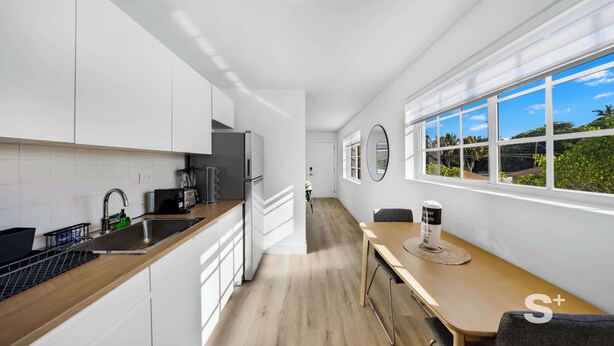 Une cuisine moderne avec des meubles blancs, un plan de travail en bois et une grande fenêtre donnant sur un paysage verdoyant.