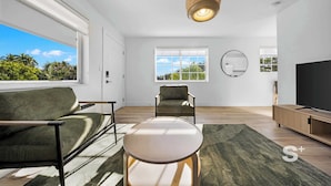 Un salon moderne avec un canapé, une table ronde, un téléviseur et une grande fenêtre donnant sur un paysage verdoyant.
