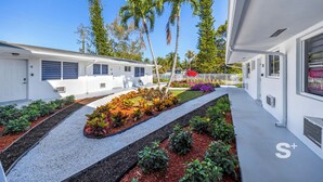 A modern building with a white exterior, a covered walkway, and a landscaped garden with various plants and a palm tree.