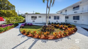 A two-story building with a white exterior, numbered rooms, and a central garden with a palm tree. - Stylish 1-BD Apt  | Gym, BBQ, Free Parking (Miami)