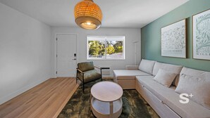 A modern living room with a sofa, a chair, a round table, and a hanging light fixture. - Stylish 1-BD Apt  | Gym, BBQ, Free Parking (Miami)