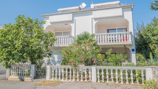 Ein zweistöckiges Gebäude mit Balkonen, einem verschlossenen Eingang und umgebender Bepflanzung.