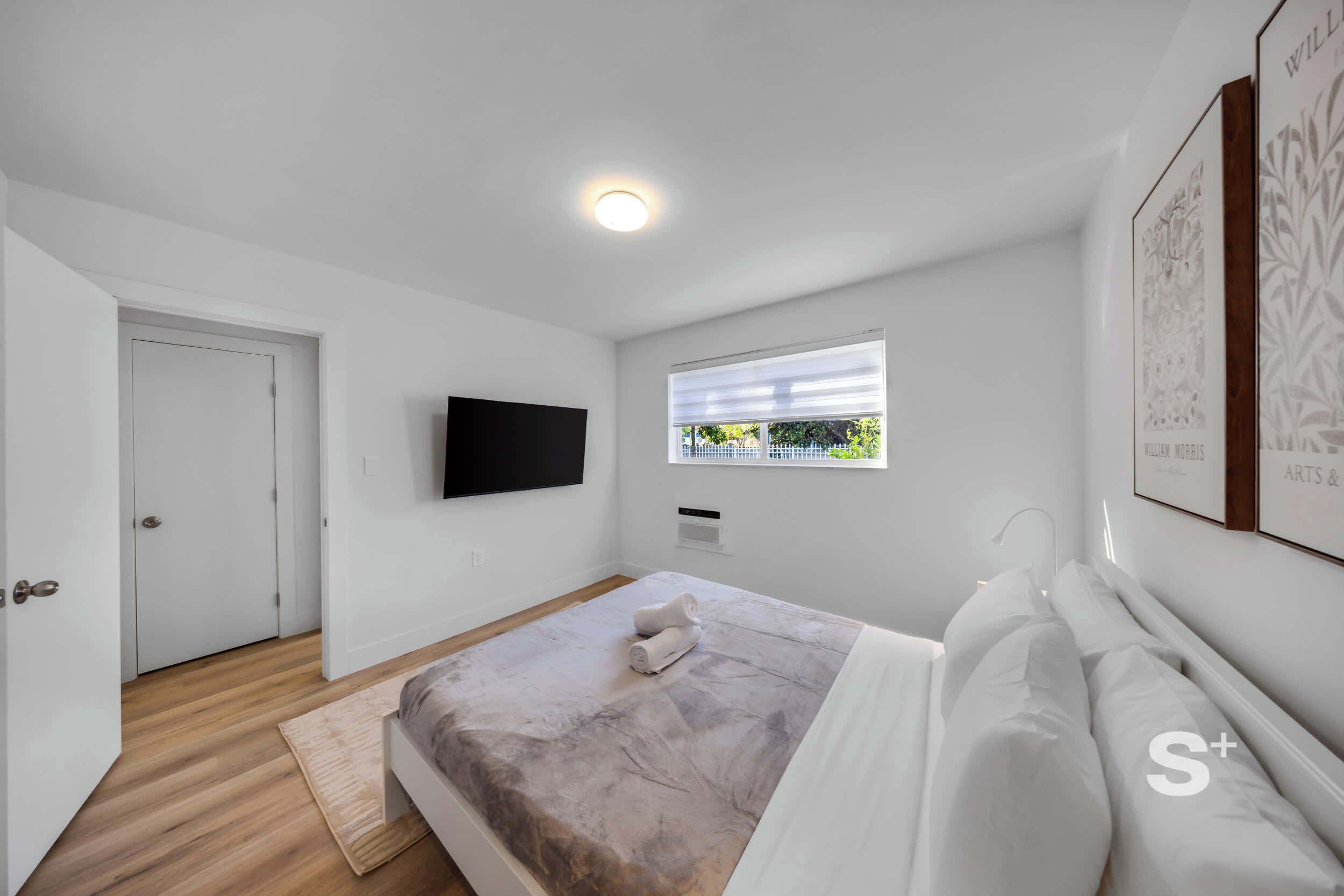 Une chambre à coucher avec un lit, un téléviseur fixé au mur, une fenêtre et une porte.