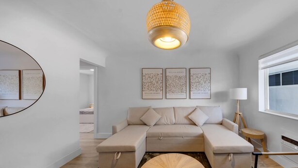 Ett modernt vardagsrum med en beige hörnsoffa, ett runt soffbord i trä och en hängande lampa.
