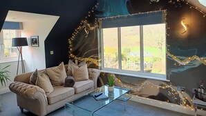 A cozy living room with a dark ceiling, a large window, and string lights. - Romantic Chalet- Hot Tub- Games Room-stream-views (Longhope)