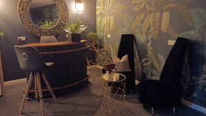 A room with a curved reception desk, a black chair, a small round table with a plant, and a wall mural of foliage. - Romantic Chalet- Hot Tub- Games Room-stream-views (Longhope)
