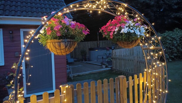 A wooden fence with string lights and flower baskets. - Romantic Chalet- Hot Tub- Games Room-stream-views (Longhope)