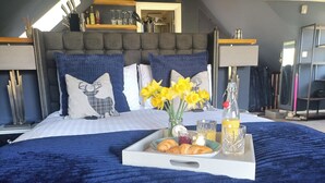 A neatly made bed with a blue blanket, a tray with croissants, jam, and juice, and a vase with yellow flowers. - Romantic Chalet- Hot Tub- Games Room-stream-views (Longhope)