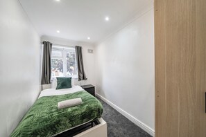 A small, modern bedroom with a single bed, a window with curtains, a radiator, and a wooden wardrobe. - 3-bed - Sleeps 5 - Pets - Parking (Northolt)