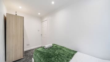 Una habitación pequeña y limpia con una cama individual, un armario y una puerta.