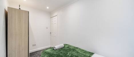 A small, clean room with a single bed, a wardrobe, and a door.