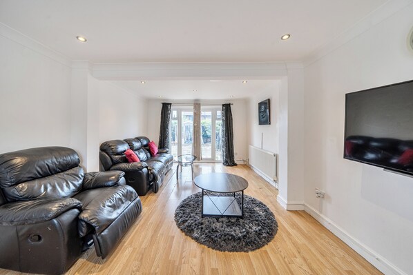 A modern living room with a leather sofa, a round coffee table, and a large TV on the wall.