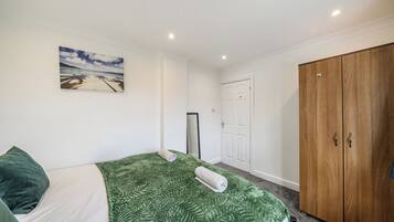 Une chambre à coucher avec un lit, une couvre-lit à motifs verts, un tableau représentant une scène de plage, une armoire et une porte.