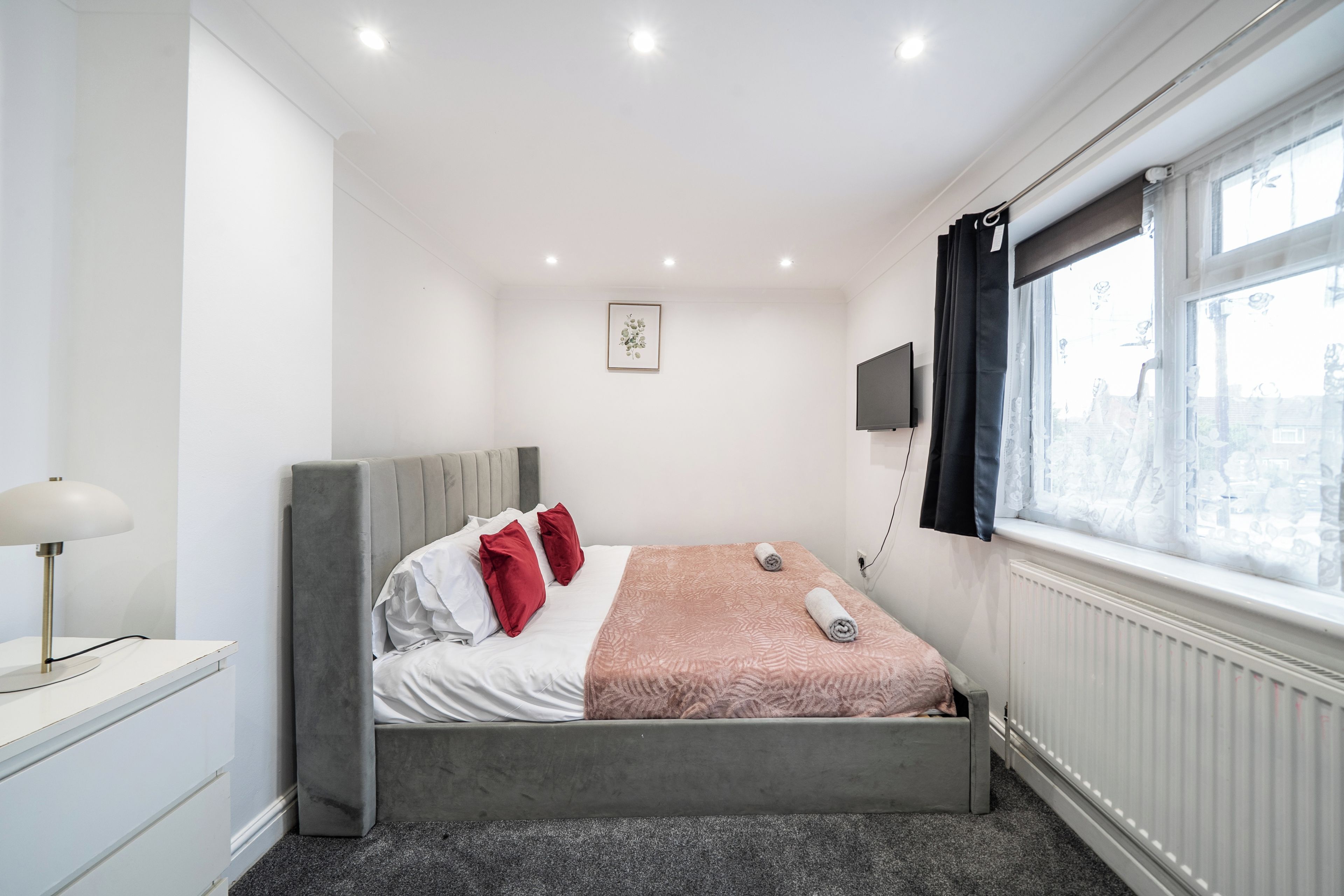 Quarto de hotel moderno com cama, luminária, televisão de tela plana e janela com cortinas.