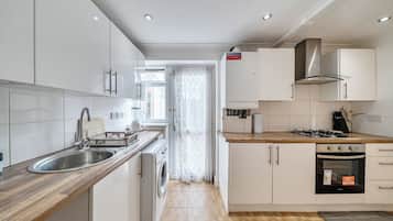 Una cocina moderna con armarios blancos, un lavamanos de acero inoxidable, lavadora integrada y estufa a gas.