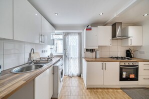 A modern kitchen with white cabinets, a stainless steel sink, a built-in washing machine, and a gas stove. - 3-bed - Sleeps 5 - Pets - Parking (Northolt)