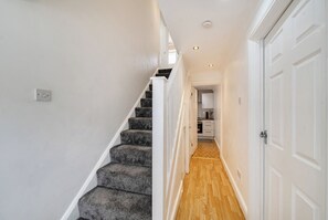 A staircase leading to a kitchen with white cabinets and a wooden floor. - 3-bed - Sleeps 5 - Pets - Parking (Northolt)