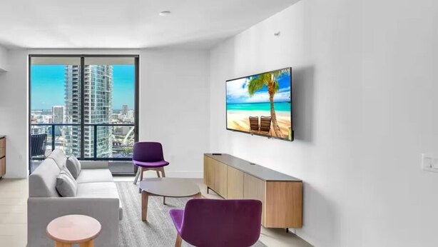 A modern living room with a sofa, two purple chairs, a coffee table, and a TV on the wall. - 2-bedroom condo in amazing Miami with fitness room, AC, WiFi, heated pool (Miami)
