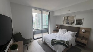 A modern hotel room with a large bed, a desk with a chair, a TV, and a balcony with a city view. - 2-bedroom condo in amazing Miami with fitness room, AC, WiFi, heated pool (Miami)