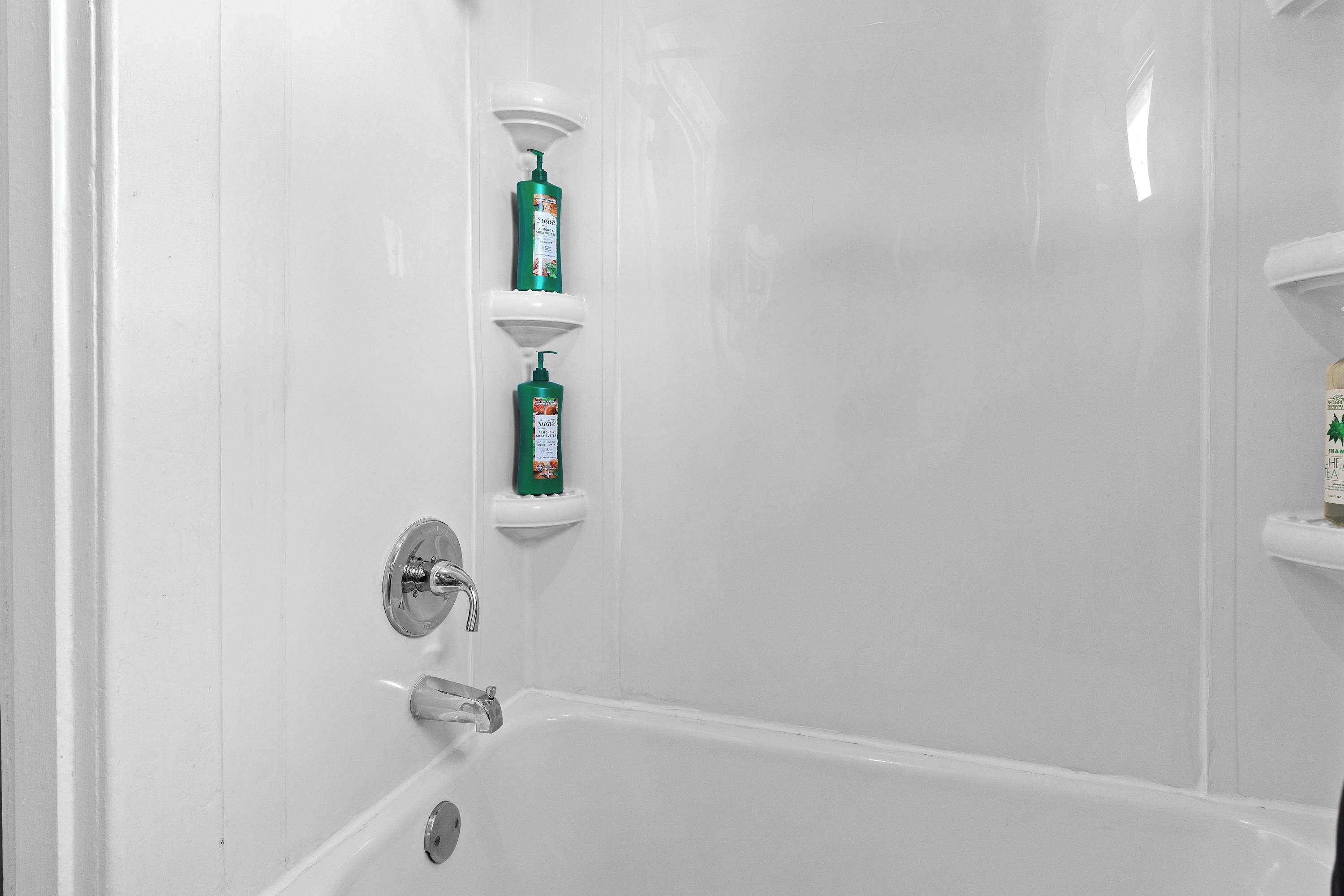 A white bathtub with a chrome faucet and a single shelf above it holding two green bottles.
