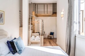 A bedroom with a bed, a chair, a staircase, and a hanging light fixture. - Domus Sabina - Central Rome (Roma)