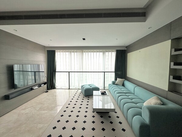 A modern living room with a large sofa, a coffee table, and a flat-screen TV mounted on the wall.
