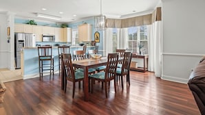 A modern kitchen with white cabinets, a stainless steel refrigerator, and a dining area with wooden chairs and a table. - Magnolia Pointe Unit 301 (Myrtle Beach)