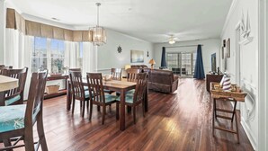 A spacious living area with a dining table and chairs, a sofa, and a large window with curtains. - Magnolia Pointe Unit 301 (Myrtle Beach)