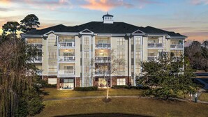 A multi-story hotel with a central courtyard, a swimming pool, and a pond. - Magnolia Pointe Unit 301 (Myrtle Beach)