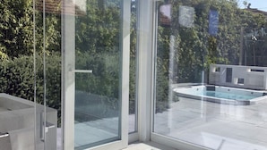 A modern bathroom with a glass shower enclosure, a bathtub, and a view of a swimming pool and greenery outside. - Elegant beachfront villa with jacuzzi, garden, and panoramic terrace. (Montignano-Marzocca)