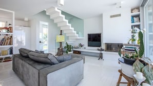 A modern living room with a grey sofa, a staircase, a flat-screen TV, and a bookshelf. - Elegant beachfront villa with jacuzzi, garden, and panoramic terrace. (Montignano-Marzocca)
