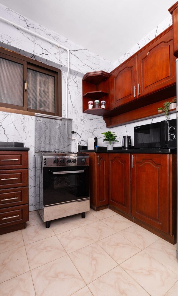 A compact kitchen with a built-in oven, microwave, and wooden cabinets. - Xuru Stays I The 2 BDR Sterling Residence 5 min to CAI Airport (Cairo)