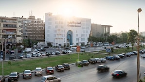 Una concurrida calle urbana con un edificio blanco destacado, que cuenta con una amplia entrada en arco y señalización que dice 'Oriental Weaver'.