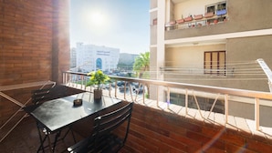 Un balcón con una mesa y sillas, una planta en maceta y vistas a un edificio con balcones.