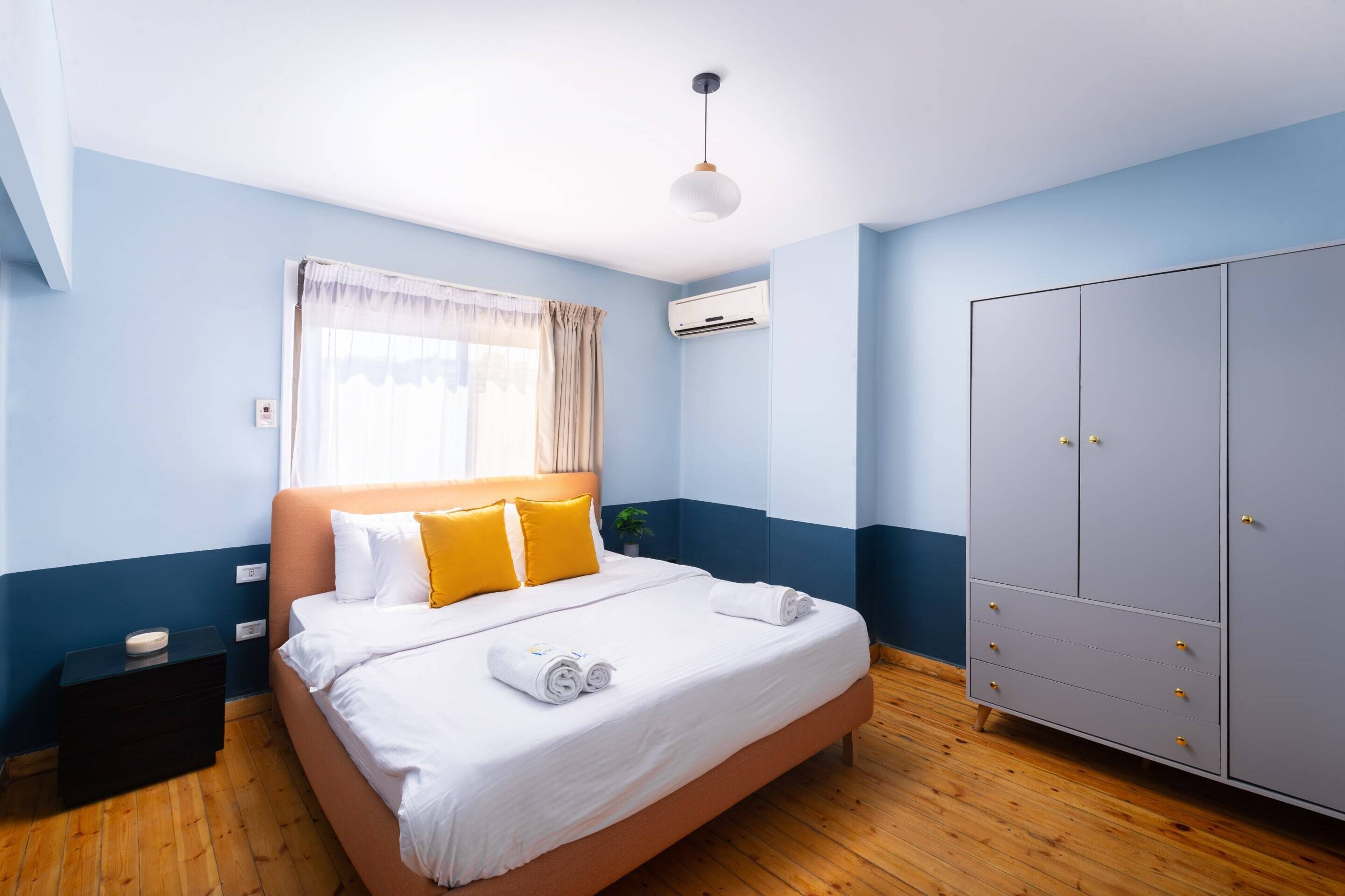 Quarto com cama, guarda-roupa, mesa de cabeceira e ar condicionado.