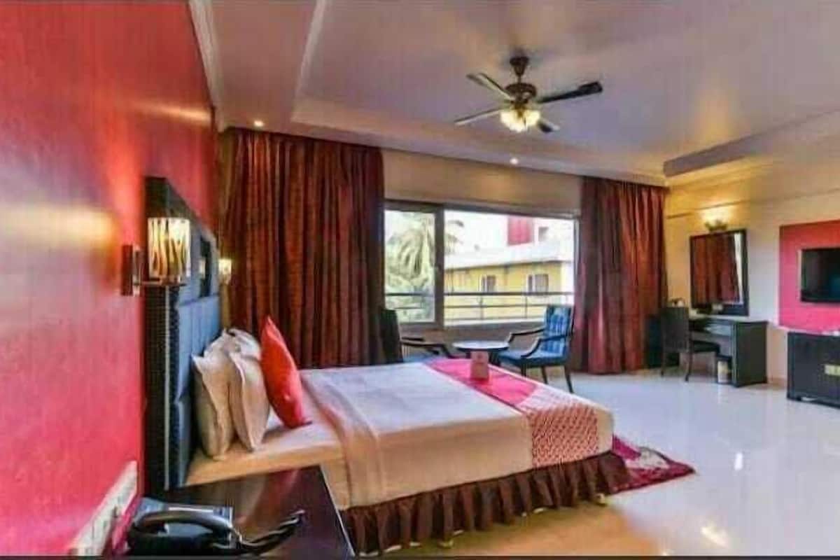 Habitación de hotel moderna con cama, escritorio, silla, televisión y vistas al balcón.