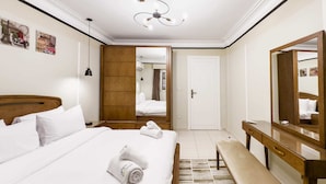 A hotel room with a large bed, a wooden bench, a desk with a mirror, and a door leading to another room. - Xuru Stays I The Hospitable 2bdr Apt. 5 min From CAI Airport (Cairo)