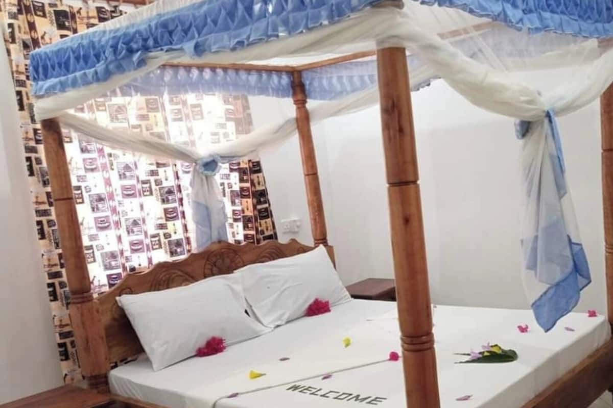A four-poster bed with a canopy, a bedside table, and a wall with patterned wallpaper.