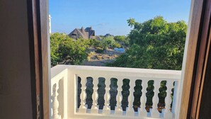 A balcony with a white balustrade overlooking a coastal area with thatched-roof buildings and lush greenery. - Diamond Luxury House Watamu (Watamu)