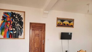 A room with a wooden door, a television mounted on the wall, and a painting of a lion's face. - Diamond Luxury House Watamu (Watamu)