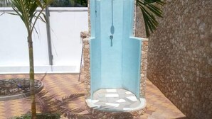 A small outdoor seating area with a light blue bench, surrounded by a stone wall and a palm tree. - Diamond Luxury House Watamu (Watamu)