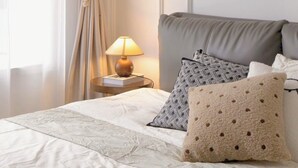 Un lit bien fait, avec une couette blanche, une tête de lit grise et deux coussins à motifs.