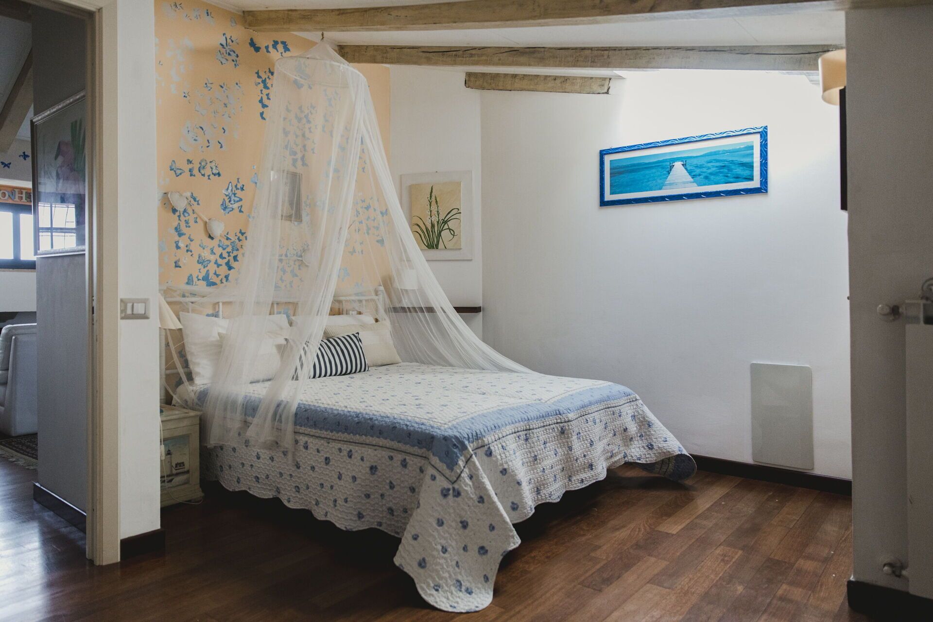 Un dormitorio con cama bajo dosel, un cuadro enmarcado en la pared y suelo de madera.