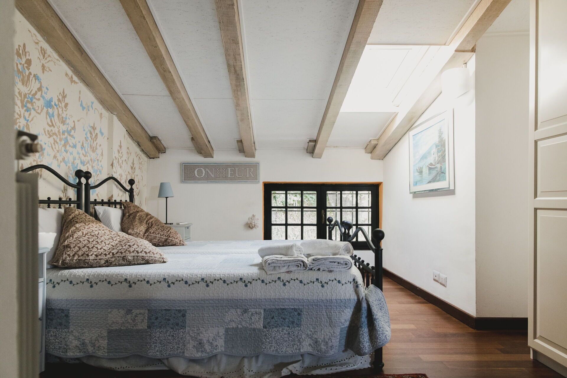 A bedroom with a bed, a nightstand, a lamp, a window, and a door.