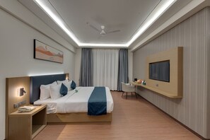 A modern hotel room with a bed, bedside table with a phone, a desk with a chair, a flat-screen TV, and a ceiling fan.