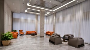 A spacious lobby with a polished marble floor, modern seating arrangements, and a large plant.