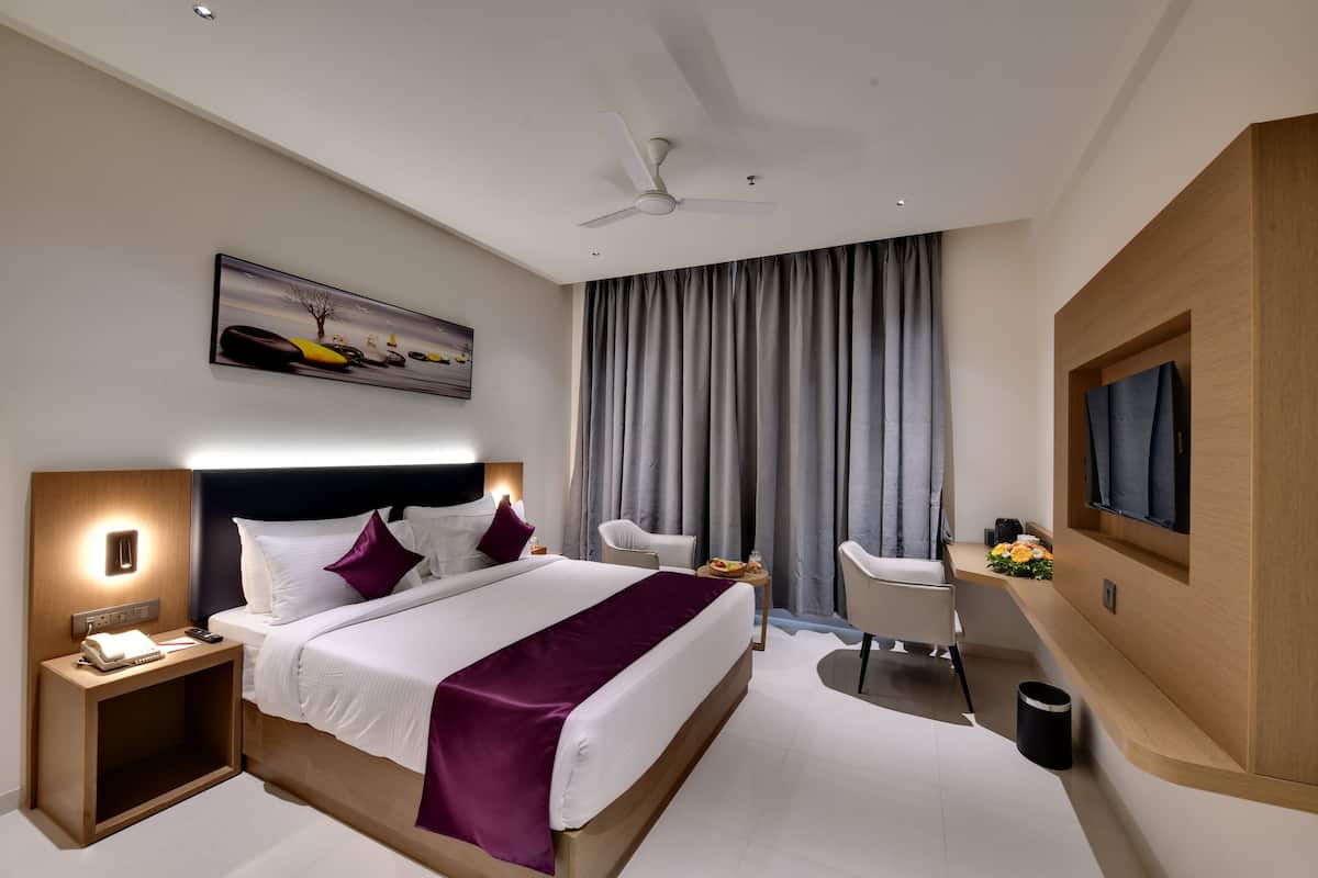 A modern hotel room with a large bed, a desk, a chair, a TV, and a ceiling fan.