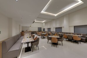 A spacious dining area with multiple tables and chairs, a long bench, and recessed ceiling lighting.